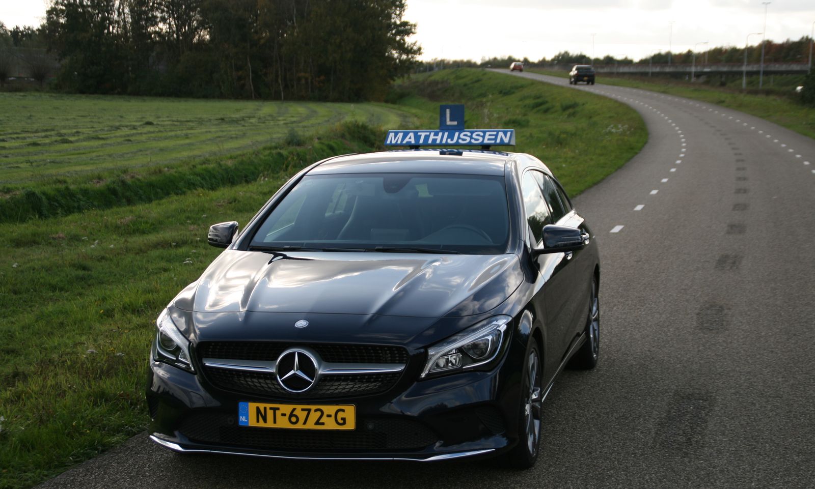 De lesauto van Autorijschool Mathijssen met blauw daklichtbord onderweg op een weg bij Etten-Leur